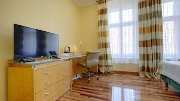A hotel room with a wooden desk, a television, a chair, and a bed.