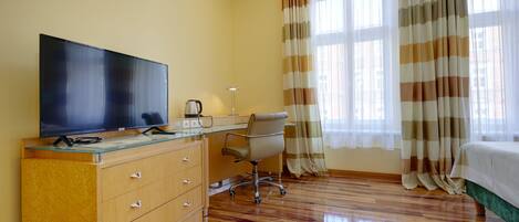 A hotel room with a wooden desk, a television, a chair, and a bed.