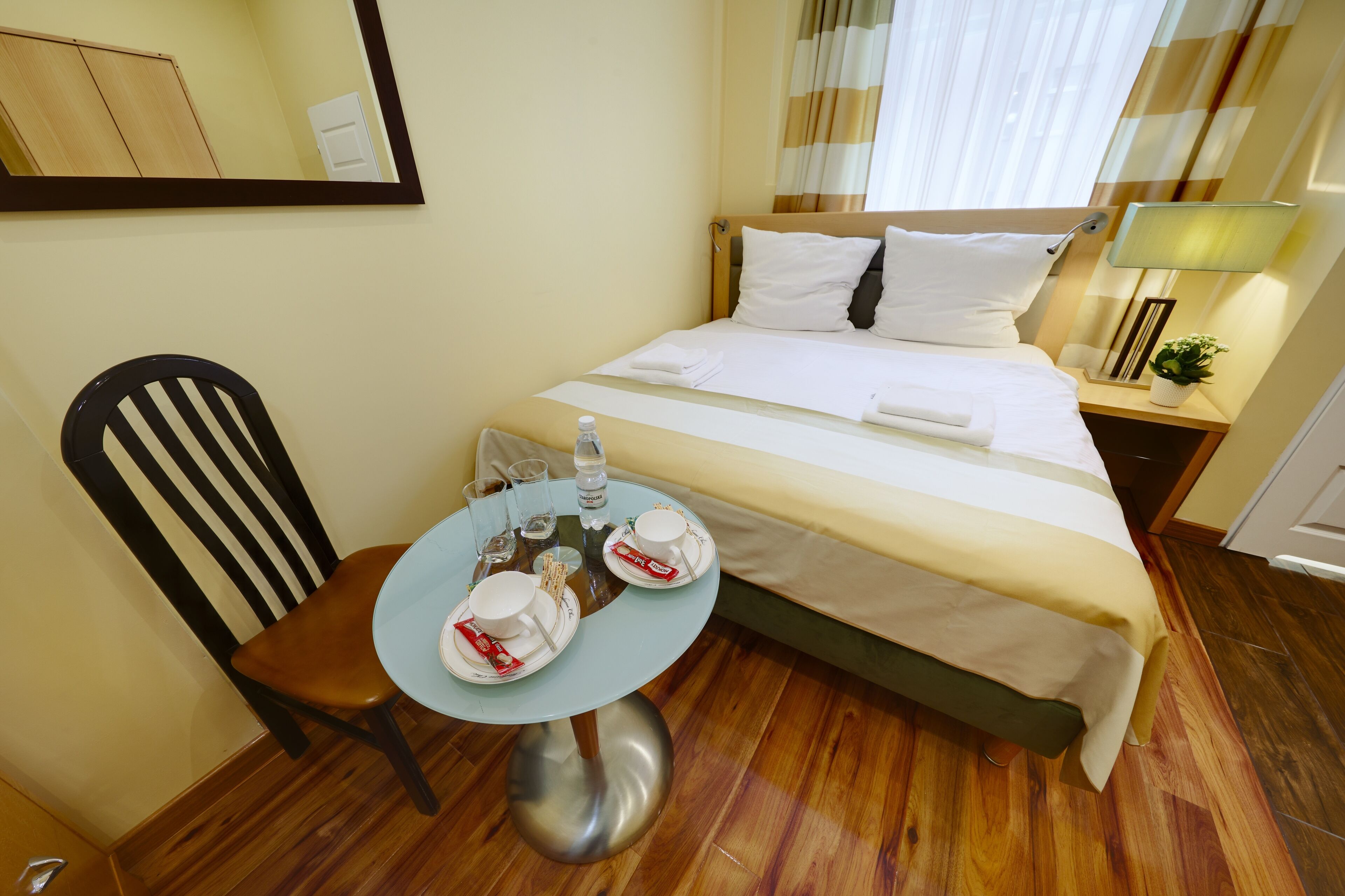 Une chambre d’hôtel avec un lit, une table avec des articles pour le petit-déjeuner, une chaise et un miroir.