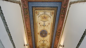 A grand staircase with ornate ceiling decorations and a view of a room with a window and curtains. - Jagiellońska 3 Apartments (Katowice)