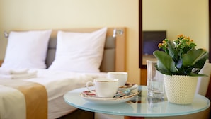 A hotel room with a bed, a glass table with a cup and saucer, a glass, and a potted plant. - Jagiellońska 3 Apartments (Katowice)