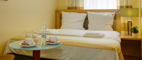 A hotel room with a neatly made bed, a small round table with breakfast items, and a window with curtains.