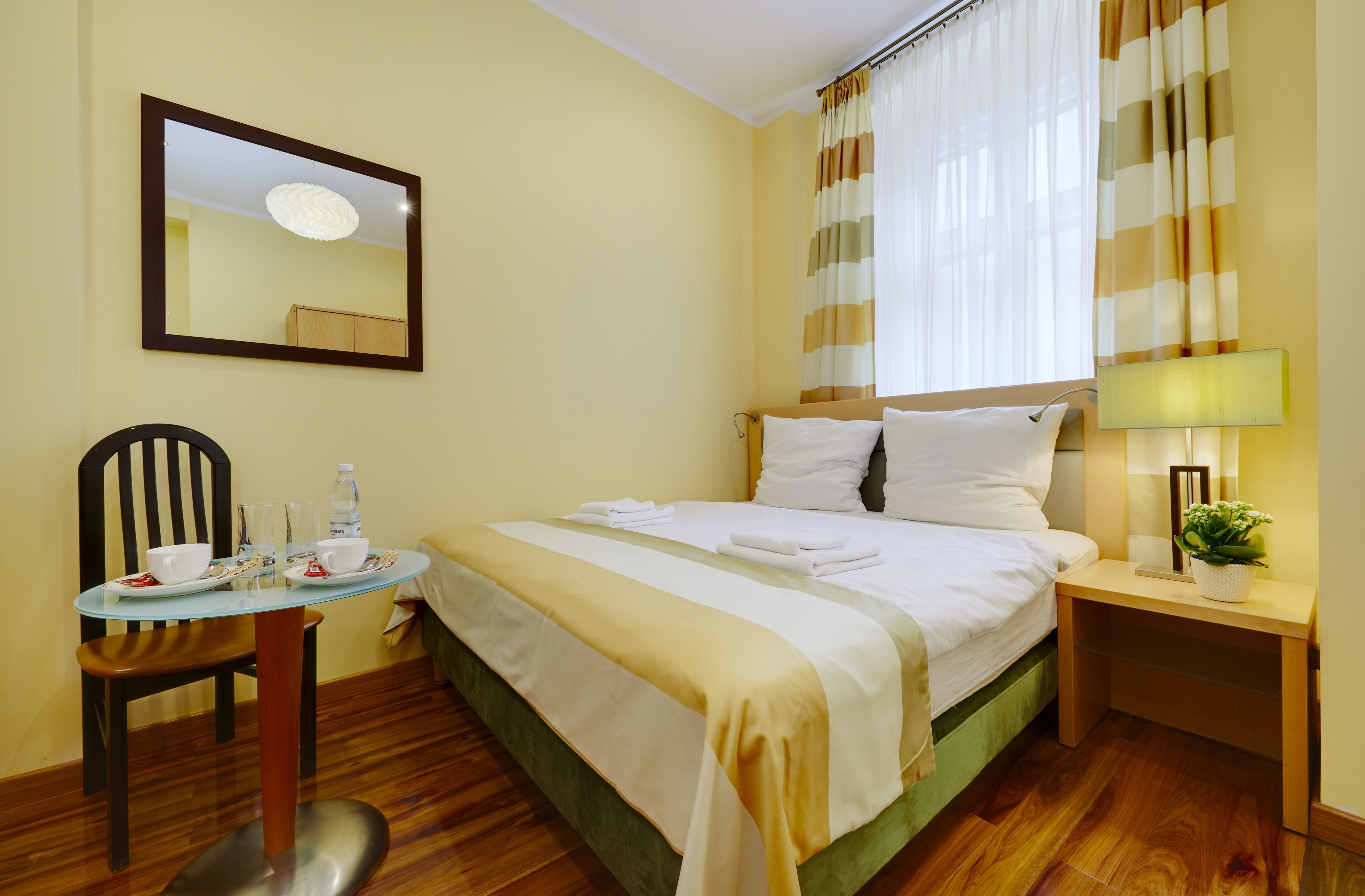 A hotel room with a bed, bedside table, chair, and a small table with a cup and saucer.