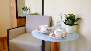 A small round table with two white cups and saucers, a glass of water, a bottle of water, and a potted plant with orange flowers. - Jagiellońska 3 Apartments (Katowice)