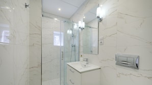 A modern bathroom with a glass-enclosed shower, a white sink, and a mirror with wall-mounted lights. - Jagiellońska 3 Apartments (Katowice)