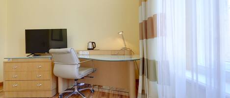 A small, modern room with a glass desk, a white office chair, a television, a coffee maker, and a wooden dresser.