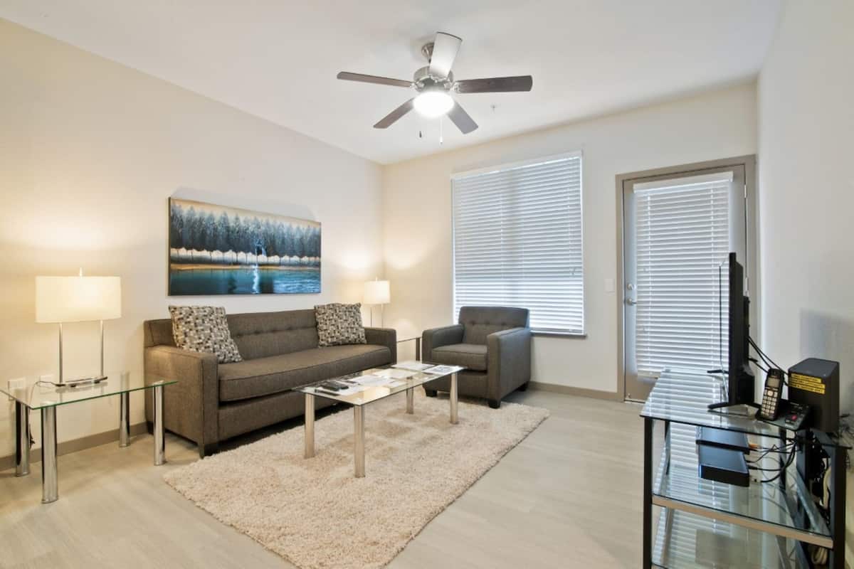 A living room with a sofa, two armchairs, a coffee table, a TV, and a ceiling fan.