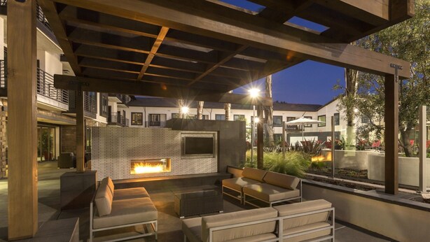Un patio al aire libre con un hogar, asientos y una pantalla de televisión.