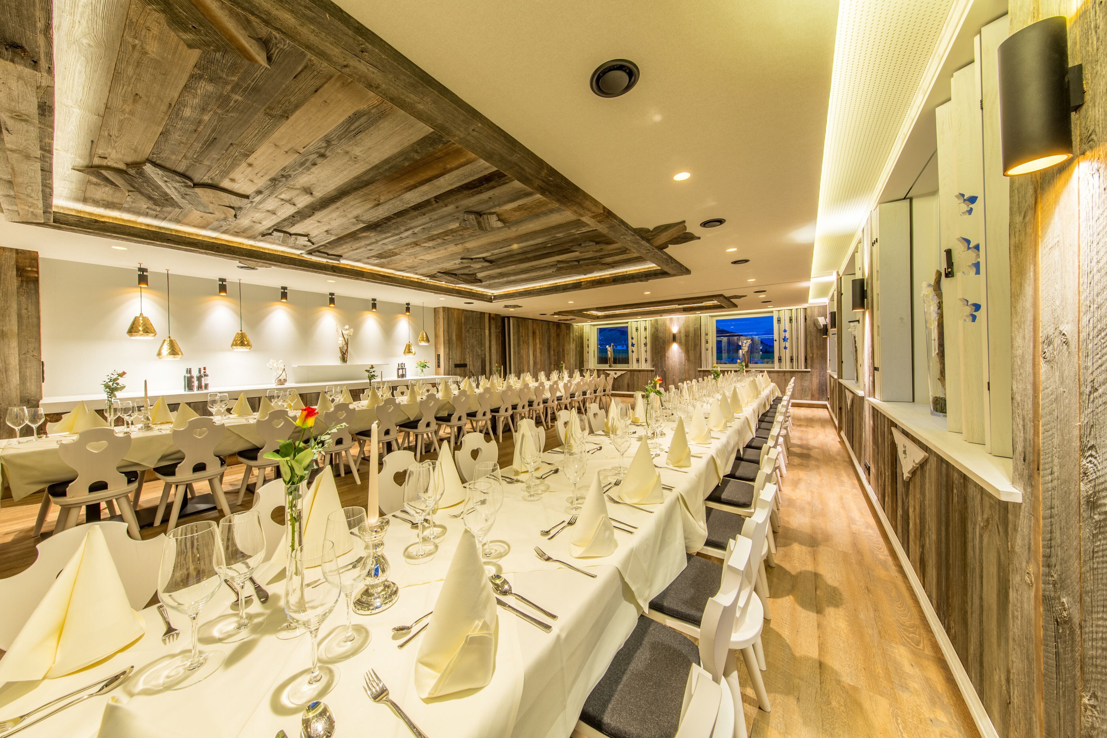 Une longue table de banquet, dressée pour un événement formel, avec des nappes blanches, des couverts en argent et de la verrerie.