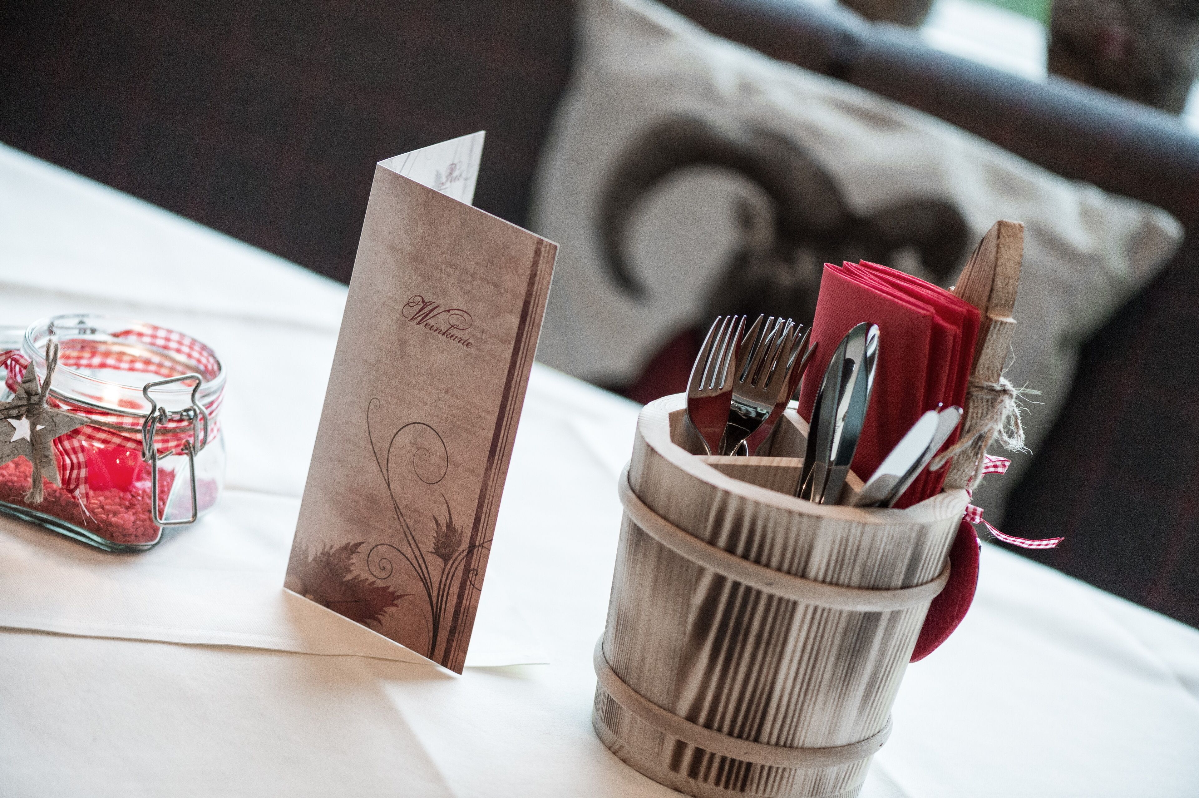 A table with a menu card, a glass jar with red items, and a utensil holder.