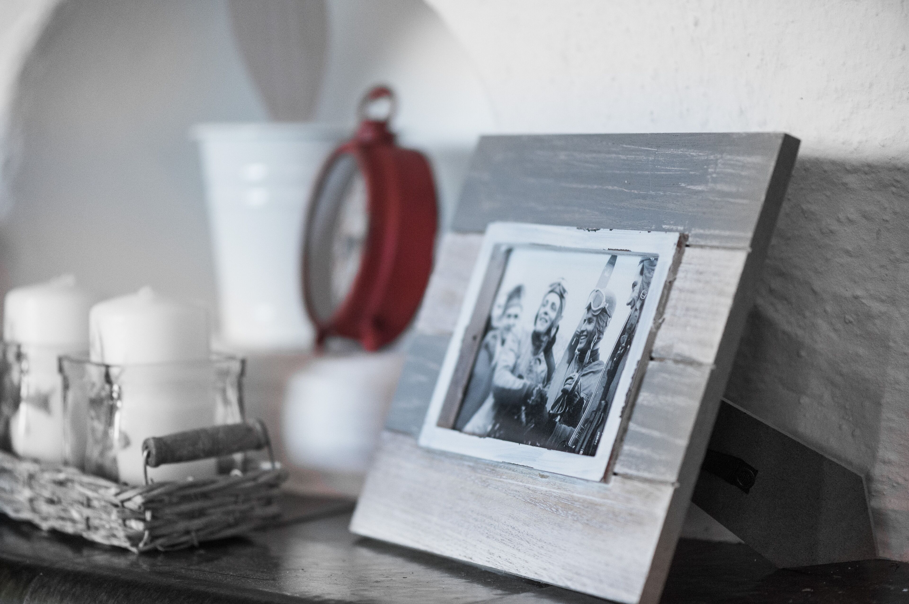 Une photographie encadrée posée sur un support en bois, une bougie blanche et un porte-bougie en verre, le tout sur une surface sombre.