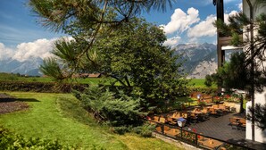 Una terraza con mobiliario exterior, rodeada de vegetación y vistas a la montaña.