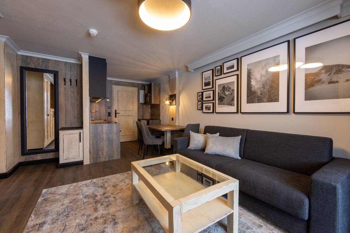 A modern living room with a grey sofa, a glass coffee table, and framed pictures on the wall.