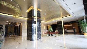 A modern lobby with a marble reception desk, a large plant, and a glass partition.