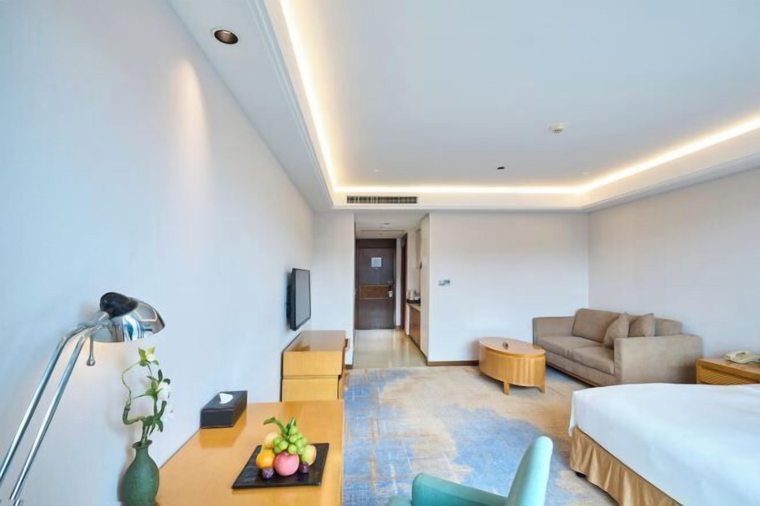 Una habitación de hotel con cama, escritorio con lámpara, sofá y televisión.
