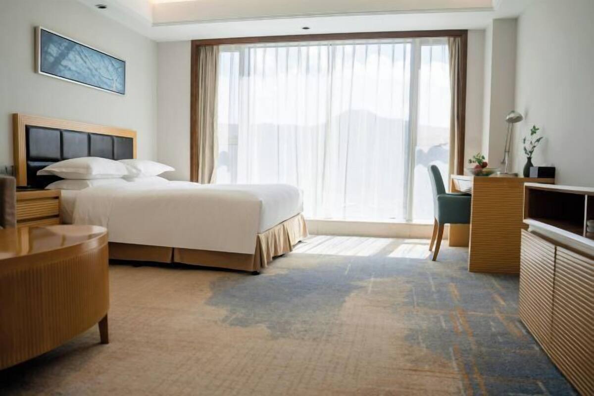 A hotel room with a bed, a desk, a chair, a TV, and a large window.