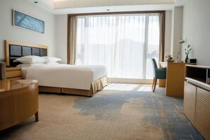 Habitación de hotel con cama, escritorio, silla, televisión y un ventanal grande.