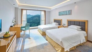 Ett hotellrum med två sängar, ett skrivbord, en stol och ett stort fönster med utsikt över bergen.