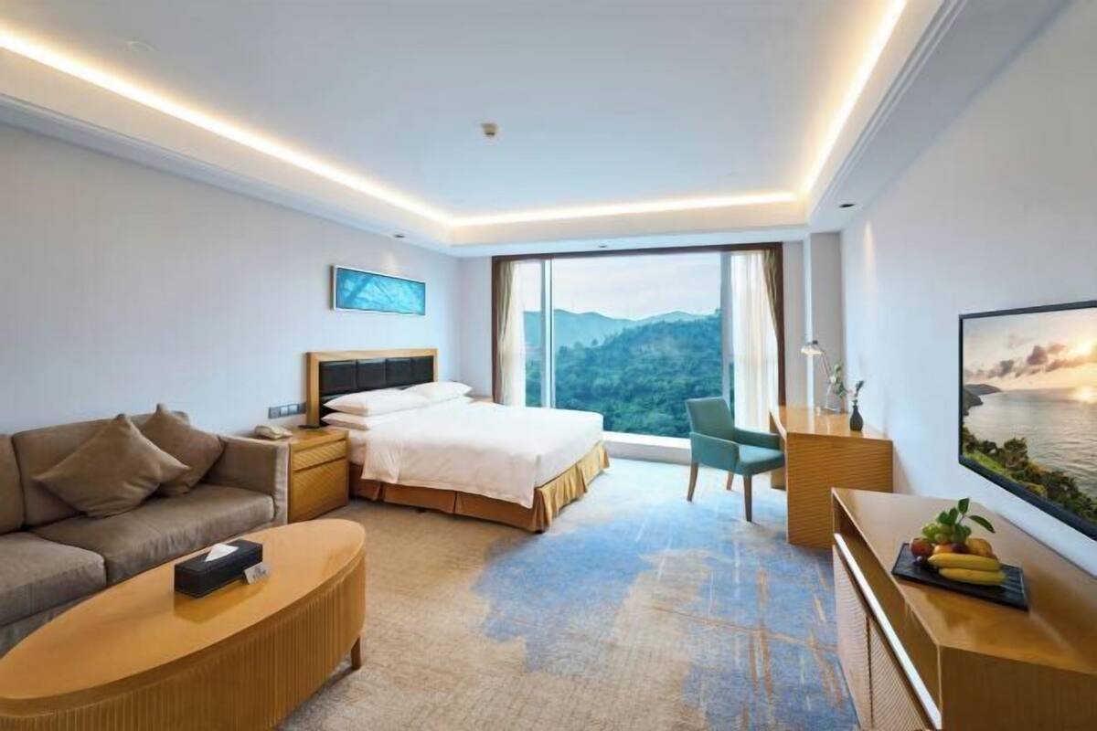 A modern hotel room with a bed, sofa, desk, and large windows offering a mountain view.