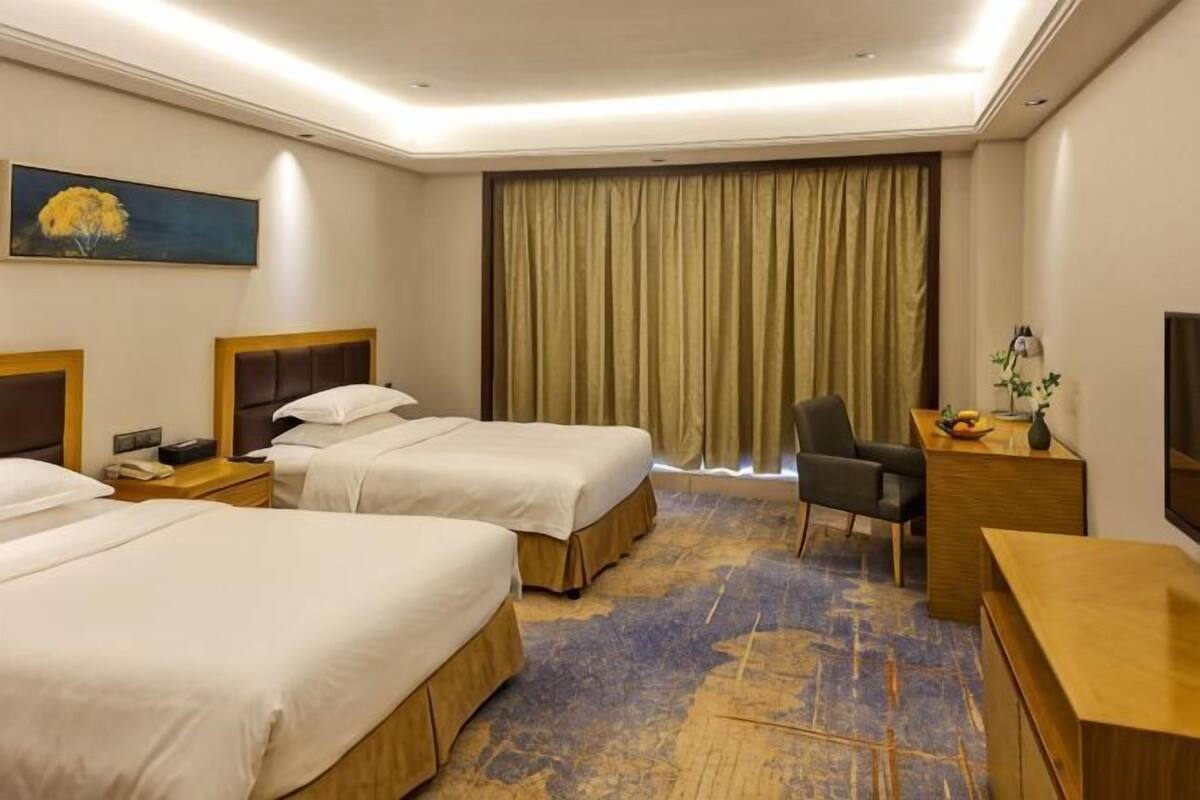 A hotel room with two beds, a desk, a chair, a nightstand, a lamp, and a large window with curtains.