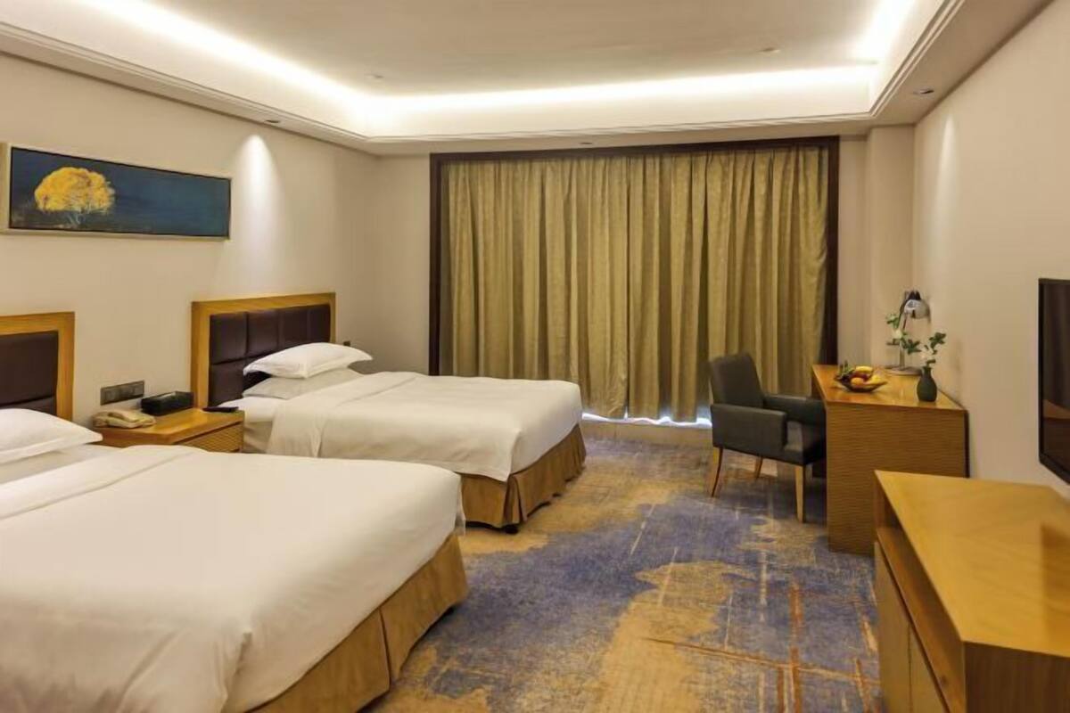 A hotel room with two beds, a desk, a chair, a desk lamp, a telephone, and a painting on the wall.