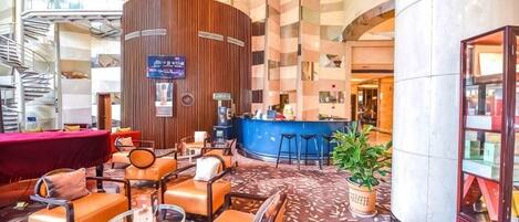 A hotel lobby with a central bar area, seating arrangements, and a staircase.