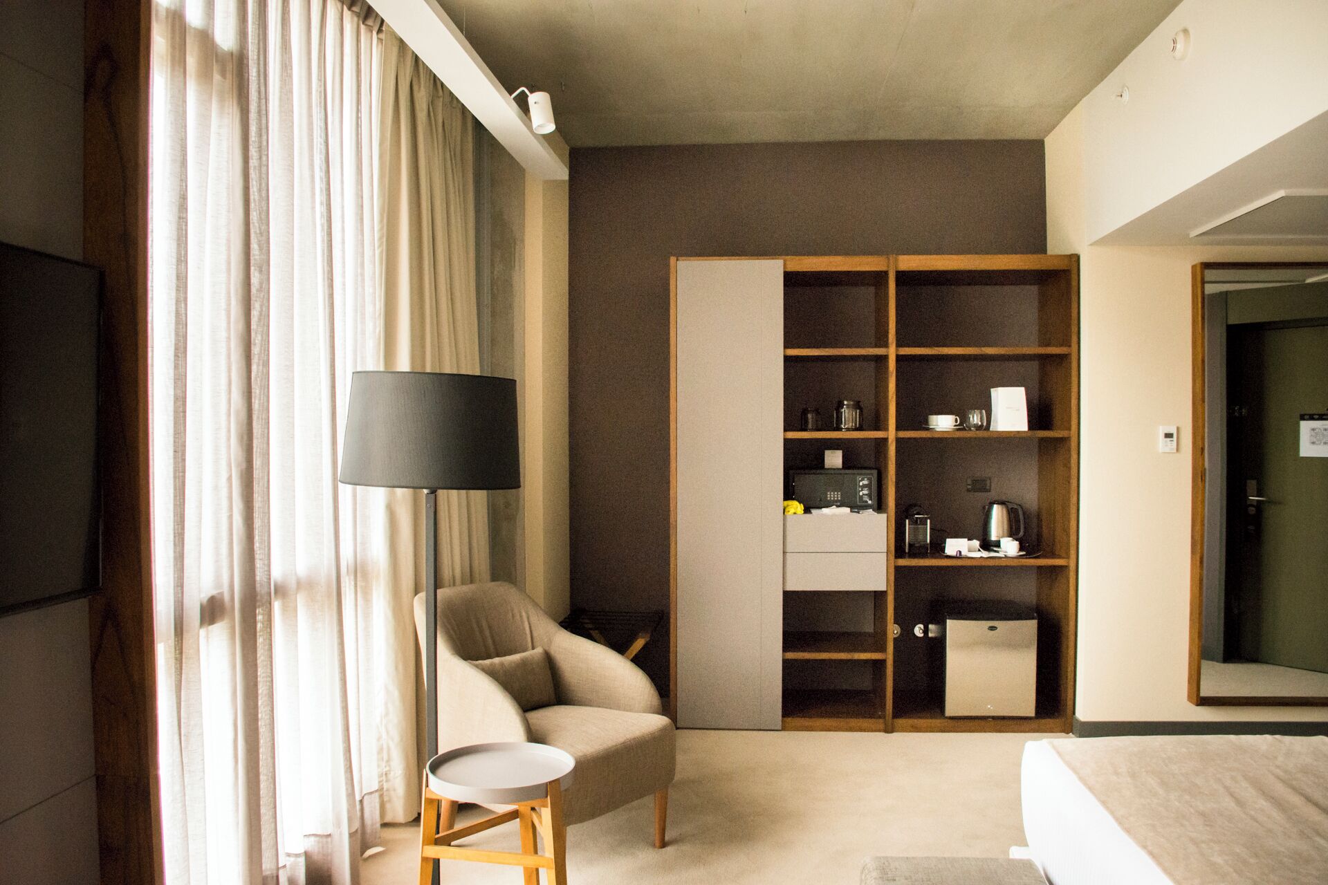 A hotel room with a bed, a chair, a desk, a wardrobe, and a television.