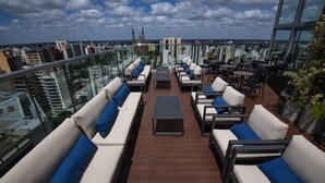 Een terras op het dak met buitenmeubilair, een glazen balustrade en uitzicht over de stad.