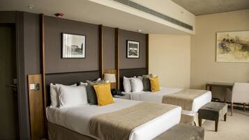 A hotel room with two beds, a desk, and a chair. There are framed pictures on the wall and a painting above the desk.