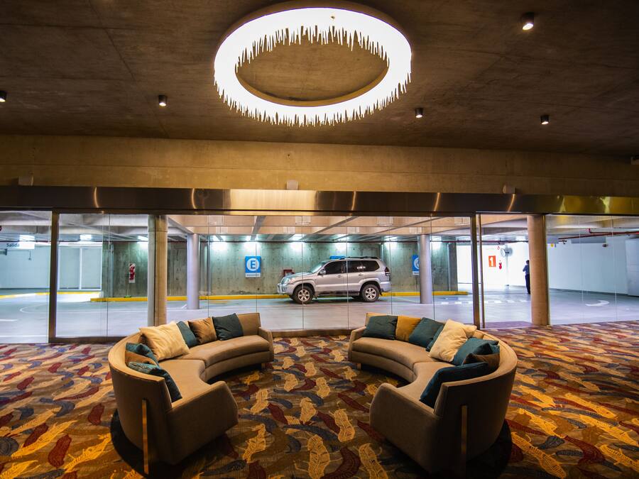Um hall com luminária circular no teto, carpete estampado e área de estar com sofás.