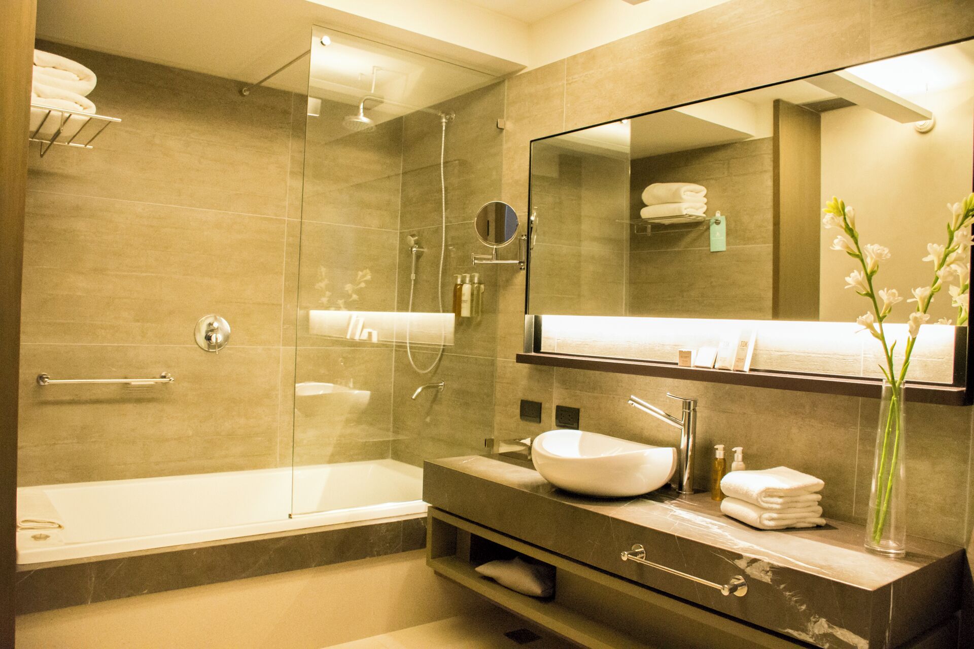 Une salle de bain moderne dotée d’une douche à parois de verre, d’un grand miroir et d’un meuble-lavabo avec un évier et un porte-serviettes.