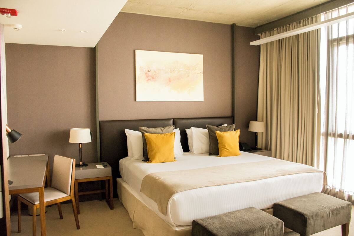 Une chambre d’hôtel avec un grand lit, un bureau avec une chaise et une fenêtre avec des rideaux.