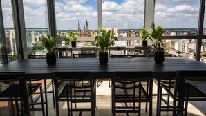 Een eetruimte met een grote tafel en stoelen, planten in potten en een uitzicht op een stadsbeeld met een opvallende kathedraal.