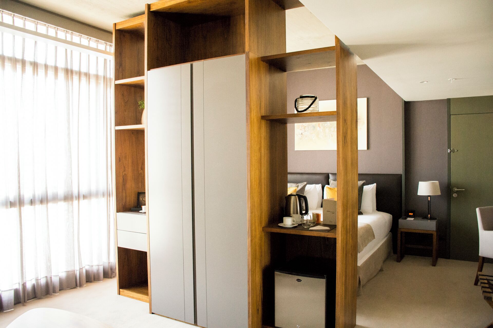 A modern hotel room with a bed, bedside table, lamp, and a wardrobe.