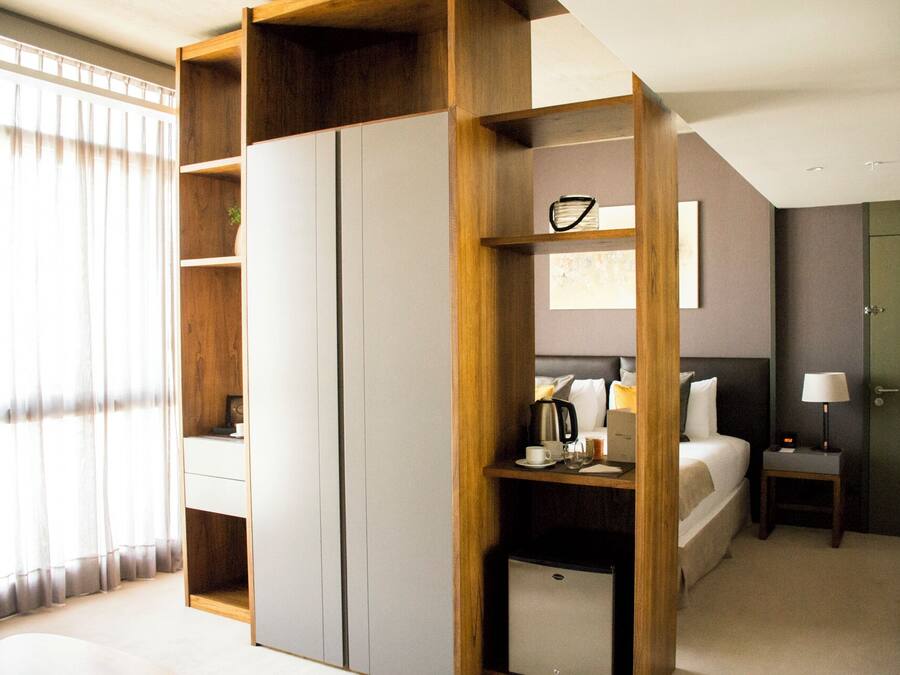 A modern hotel room with a bed, bedside table, lamp, and a wardrobe.