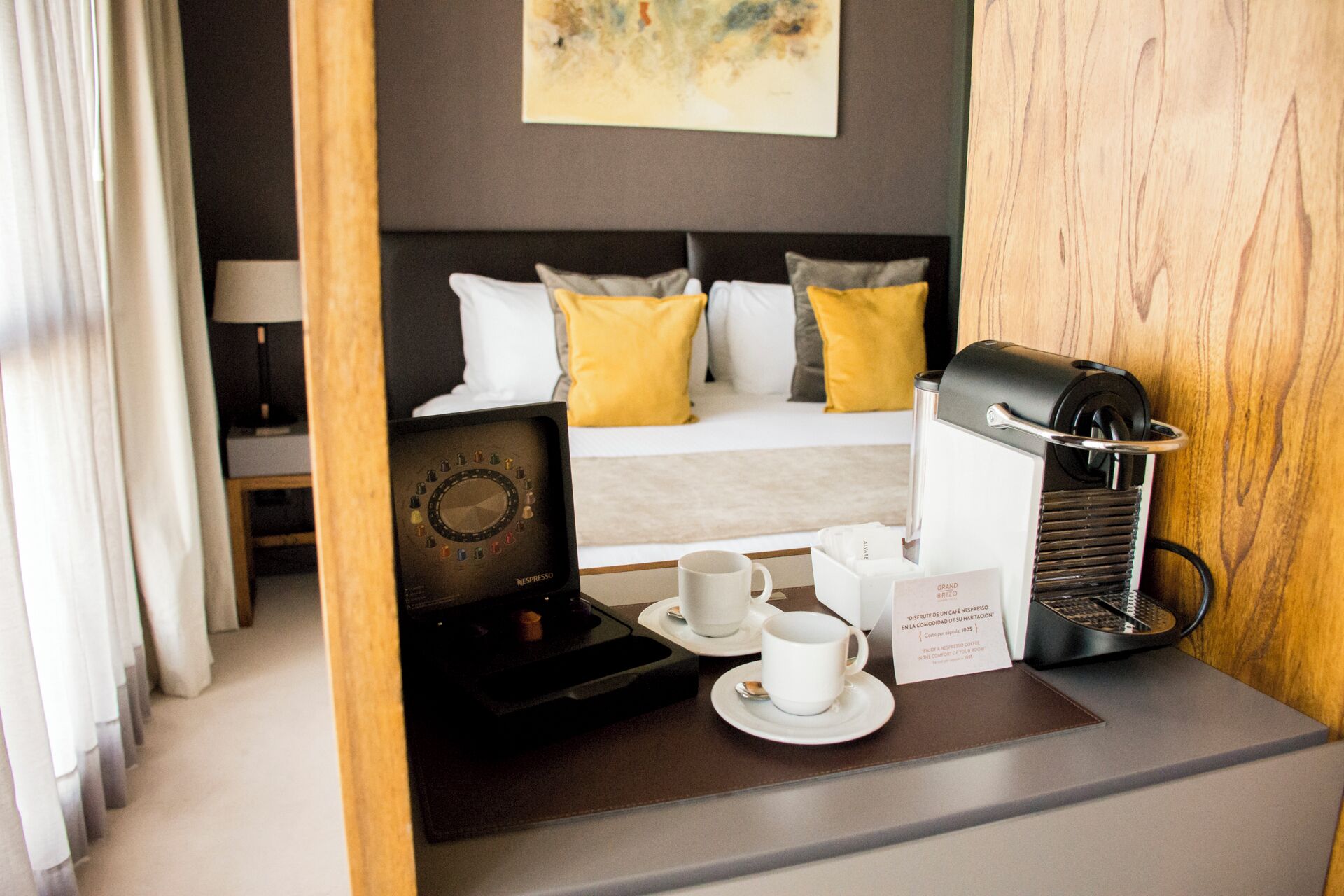 A hotel room with a bed, a coffee machine, two cups, and a menu.