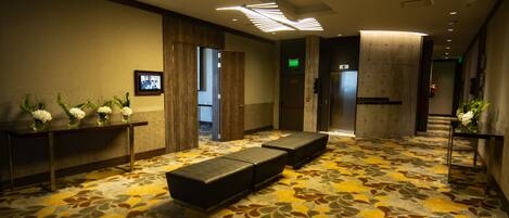 A hotel lobby with a patterned carpet, seating area, reception desk, and a television screen.