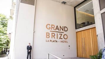 Letrero de hotel que dice "GRAND BRIZO LA PLATA - HOTEL", con un diseño moderno y un hombre de pie al frente.