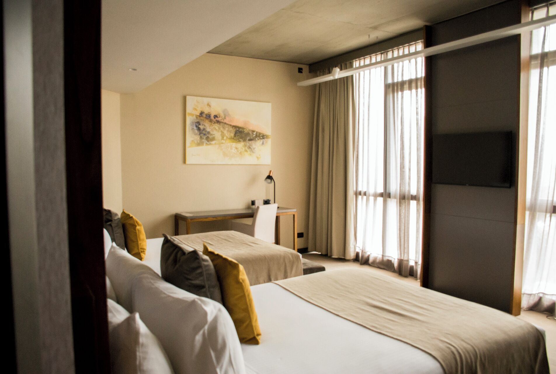 Habitación de hotel con dos camas, un escritorio, una silla, una lámpara y un cuadro en la pared.