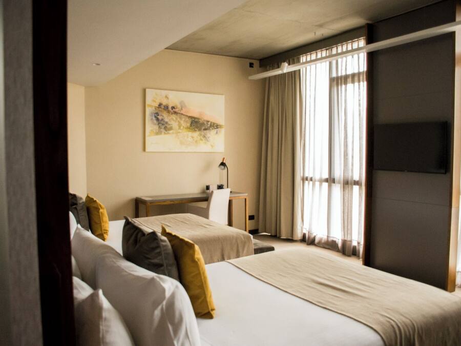 Habitación de hotel con dos camas, un escritorio, una silla, una lámpara y un cuadro en la pared.