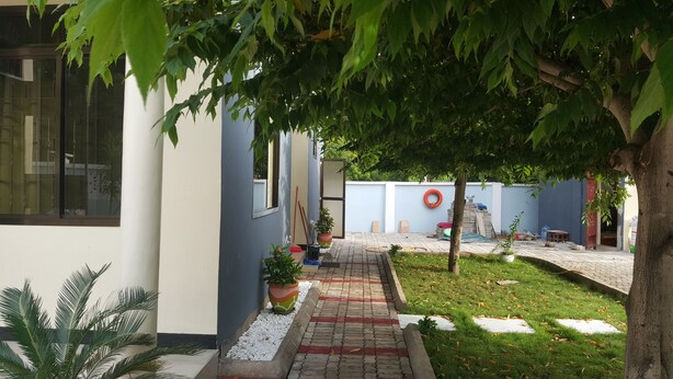 A pathway leading to a building with a blue exterior, surrounded by greenery and a small garden area. - Perfect Home Two minutes to Kijiji Beach (Dar es Salaam)