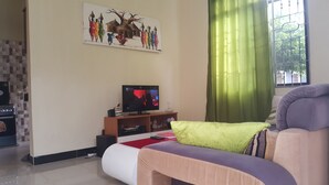 A living room with a sofa, a television, a painting on the wall, and a window with curtains. - Perfect Home Two minutes to Kijiji Beach (Dar es Salaam)