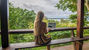 A person sitting on a wooden deck overlooking a lush green landscape and a body of water. - Treetops Lodge (Port Vila)