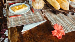 A dining table with various food items, including bread, fruits, and a cake, set on a woven placemat. - Treetops Lodge (Port Vila)