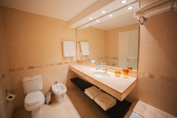 A modern bathroom with a toilet, bidet, sink, and mirror.
