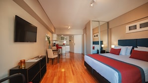 A hotel room with a bed, a desk, a chair, a TV, and a kitchen area in the background. - ARC Callao Studios & Suites (Buenos Aires)