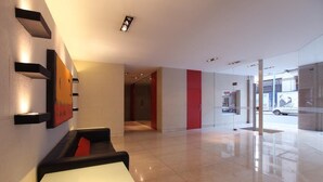 A modern lobby with a white reception desk, a black sofa with a red cushion, and a glass door leading outside. - ARC Callao Studios & Suites (Buenos Aires)