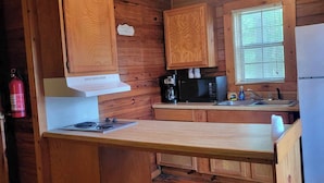 Une cuisine rustique aménagée dans une cabane en bois, équipée d’une cuisinière à gaz, d’un four à micro-ondes, d’une machine à café et d’un réfrigérateur.