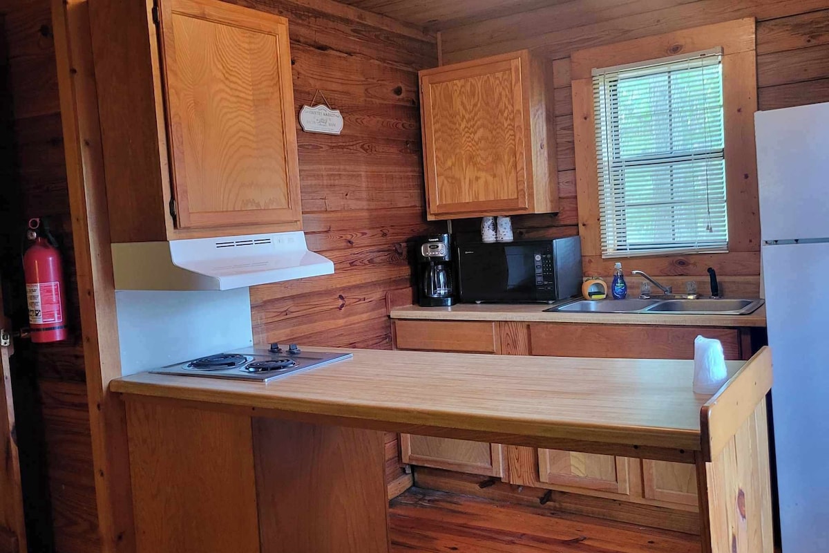 Cocina de cabaña de madera con estufa a gas, microondas, cafetera y refrigerador.