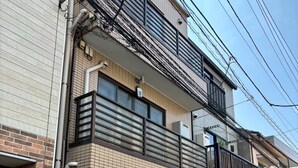 A two-story building with a brick facade, a balcony with a black railing, and multiple air conditioning units on the exterior wall. - East Shinagawa Apartment (Tokyo)